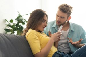 Depended woman using smartphone near angry boyfriend on couch